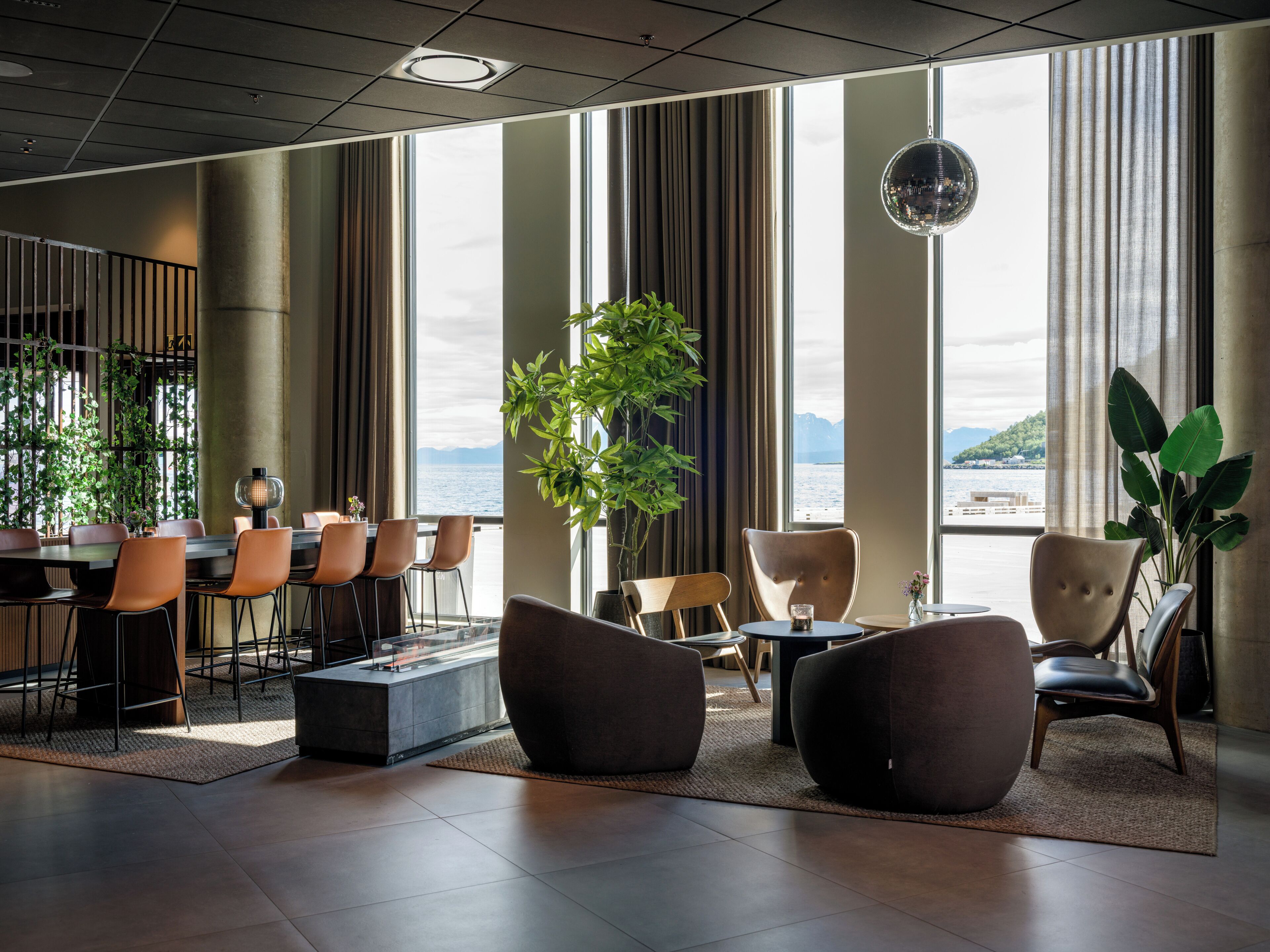 Eine moderne Hotelhalle mit großen Fenstern, Sitzgelegenheiten und Blick aufs Meer.