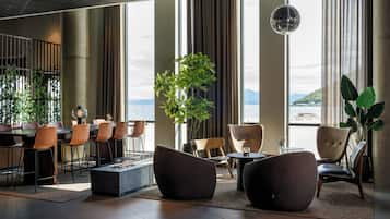 A modern hotel lobby with large windows, seating arrangements, and a view of the sea.