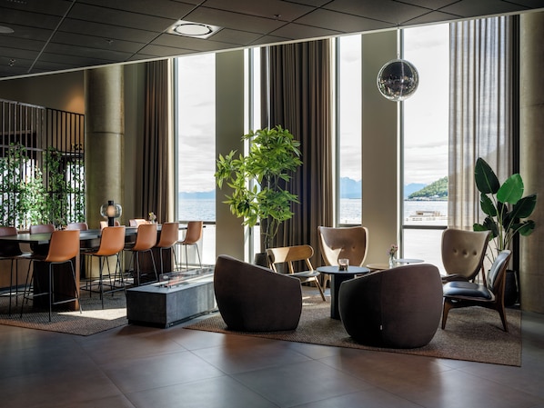 Un moderno vestíbulo de hotel con ventanas amplias, áreas de descanso y vistas al mar.