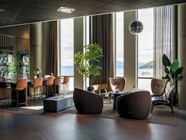 A modern hotel lobby with large windows, seating arrangements, and a view of the sea.