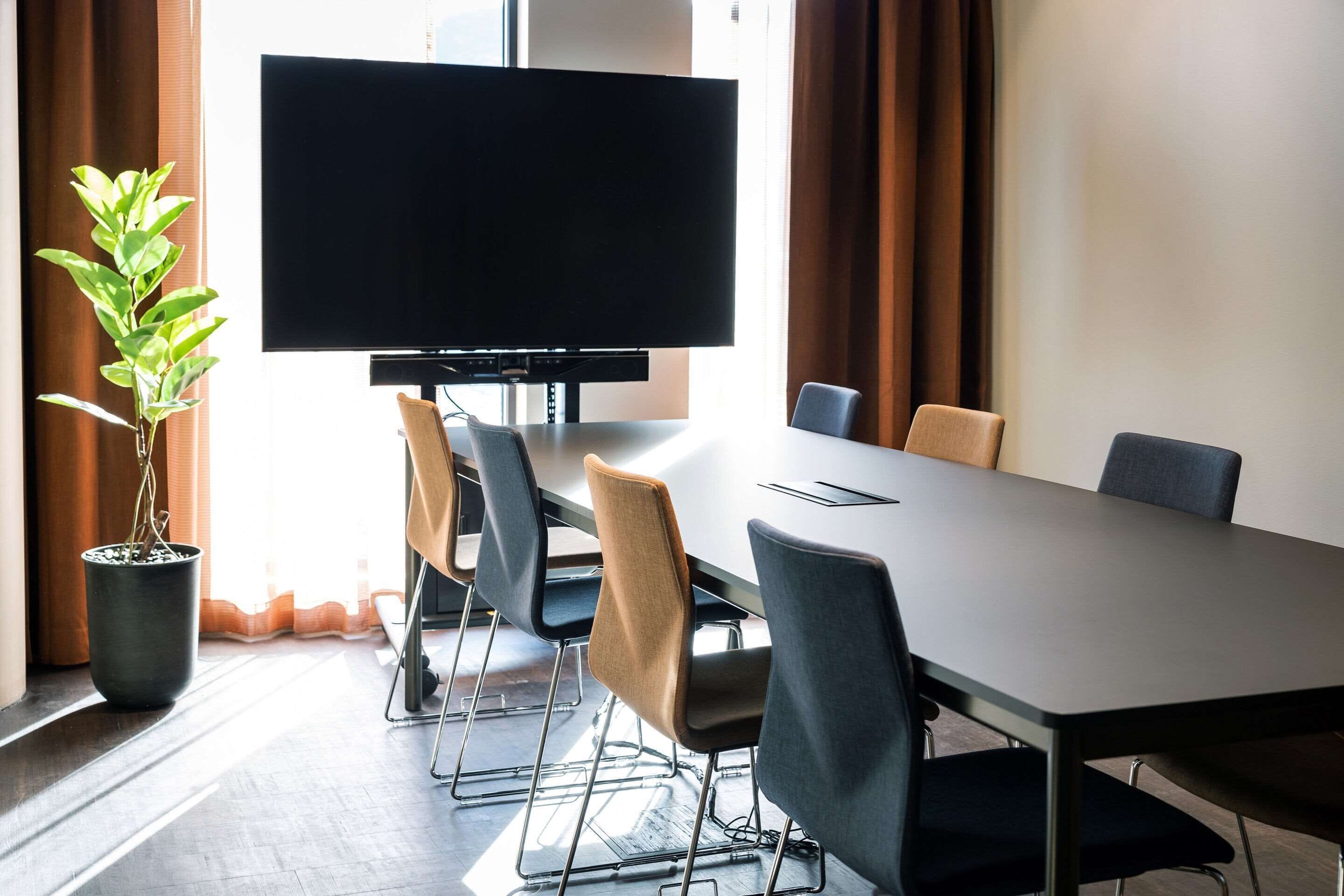 Una sala de conferencias con una televisión de pantalla grande, una mesa larga y seis sillas.