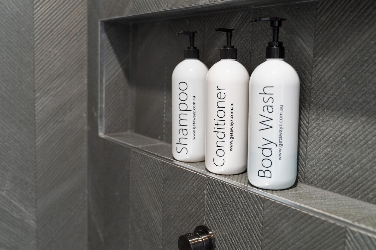Une étagère de salle de bain avec trois bouteilles de shampoing, d’après-shampoing et de gel douche.