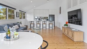 Een moderne woonkamer met een eethoek, keuken en een grote televisie aan de muur.