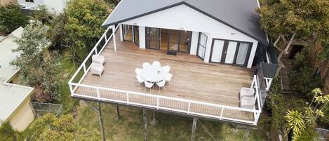 Una casa de dos pisos con un balcón, ventanas amplias y un patio con muebles de exterior.