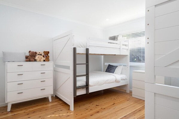 A bunk bed room with a white dresser and a window with blinds.