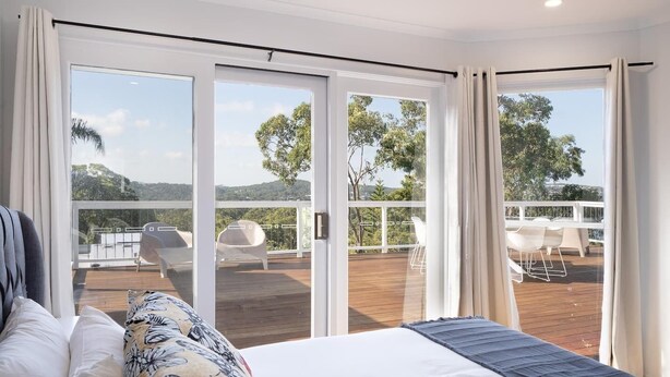 Een slaapkamer met een groot bed, uitzicht op een terras met buitenmeubilair en een schuifdeur naar een balkon.