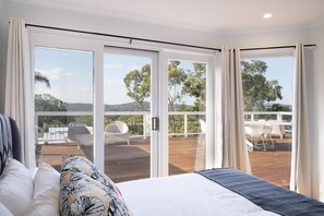 A bedroom with a large bed, a view of a deck with outdoor furniture, and a sliding glass door leading to a balcony.