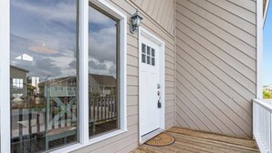Una casa con terraza de madera, puerta corrediza de vidrio y puerta blanca.