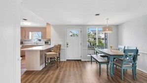 Una cocina moderna con una isla central, un comedor con mesa y sillas de madera, y vistas a través de un ventanal.