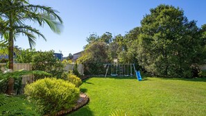 A backyard with a swing set, a palm tree, and a well-maintained lawn.