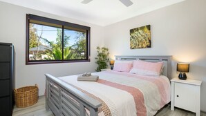 Een slaapkamer met een bed, nachtlampjes, een raam met uitzicht, een schilderij en een rieten mand.