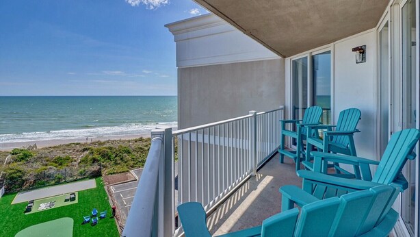 Ein Balkon mit Blick auf das Meer, türkisfarbene Stühle und eine kleine Rasenfläche mit einem Tisch.