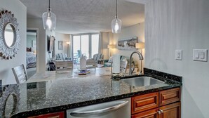 Eine moderne Küche mit einer Granitabdeckung, einer Edelstahlspüle und Holzschränken. Es gibt einen Essbereich mit gestreiften Stühlen und einem Tisch.