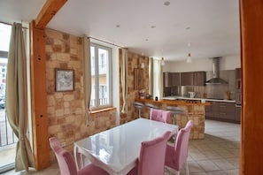 A modern kitchen with a central island, stone walls, and a dining area with pink chairs.