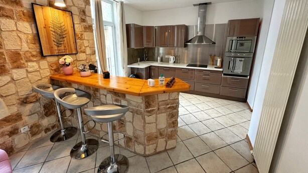 Een moderne keuken met een accentmuur van steen, barstoelen, roestvrijstalen apparatuur en een groot raam.