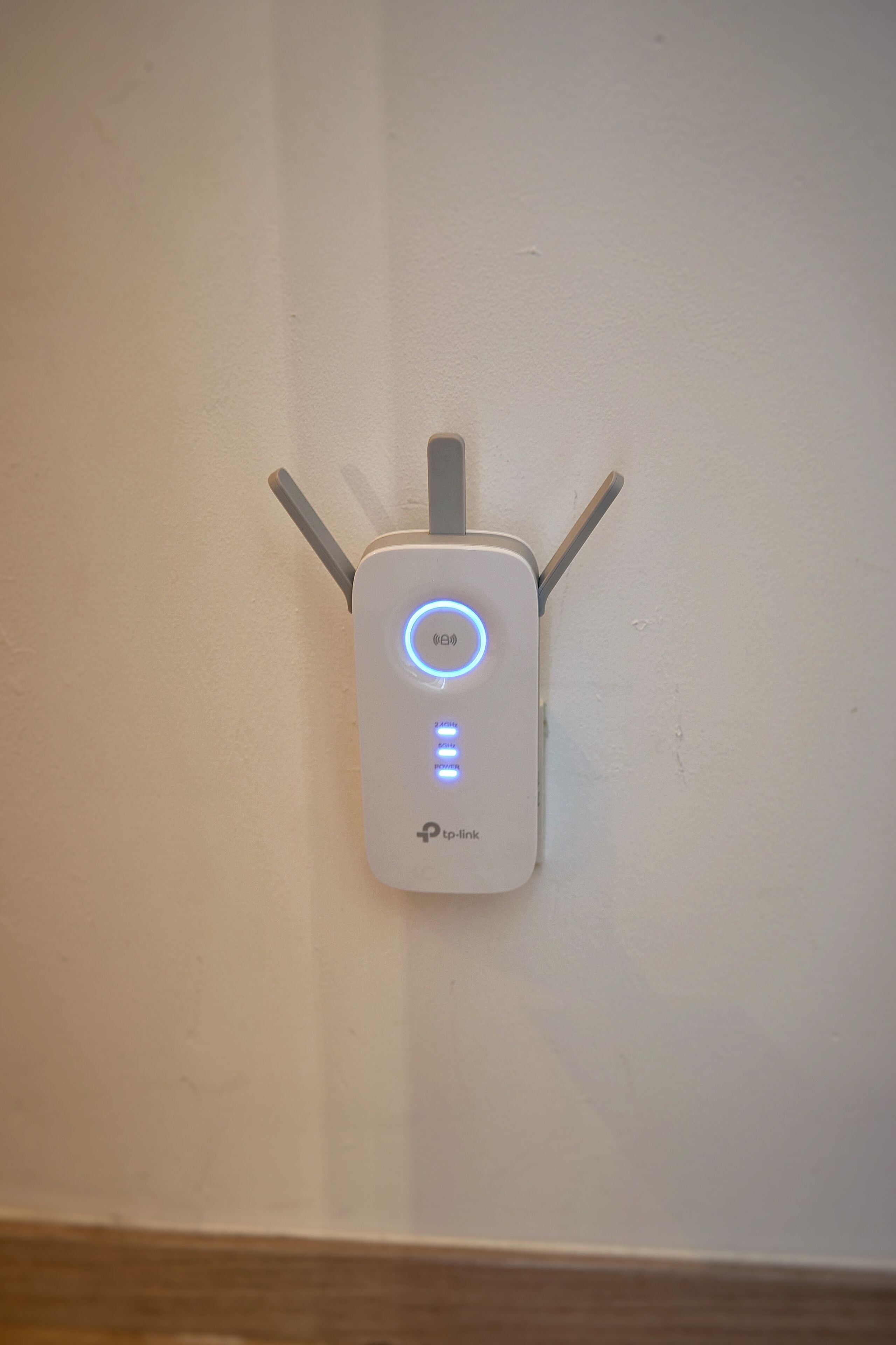 A wall-mounted device with a circular blue light and two vertical antennas.