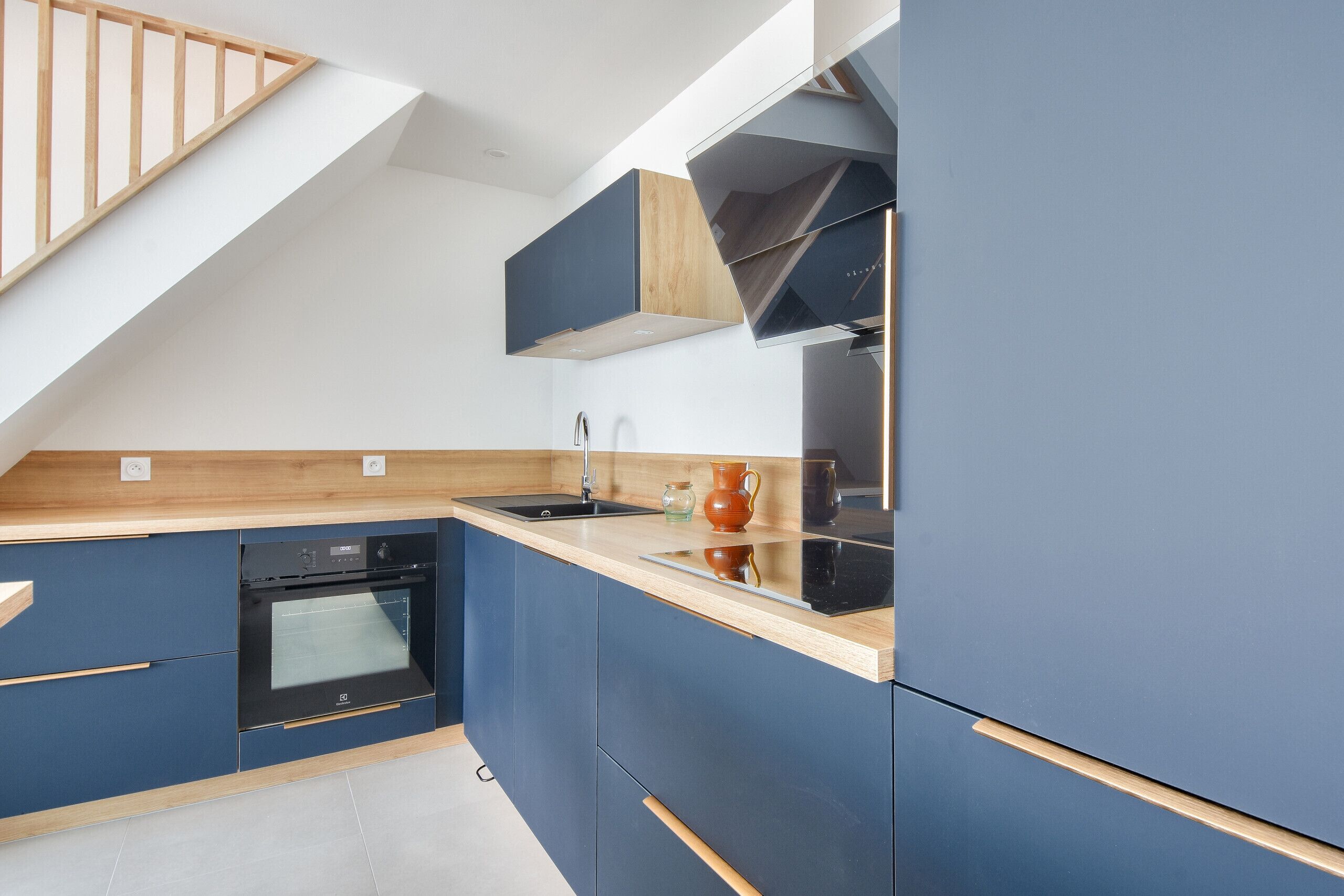 Une cuisine moderne équipée d’un four encastré, d’un évier et d’un escalier en bois.