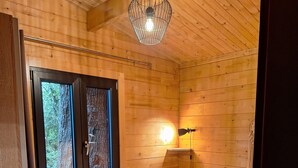 Een kleine, gezellige houten kamer met twee bedden, een raam, een hanglamp en een wandlamp.
