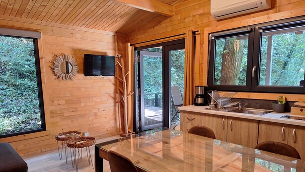 Een moderne keuken met houten kastjes, een glazen eettafel en grote ramen met uitzicht op het omliggende landschap.