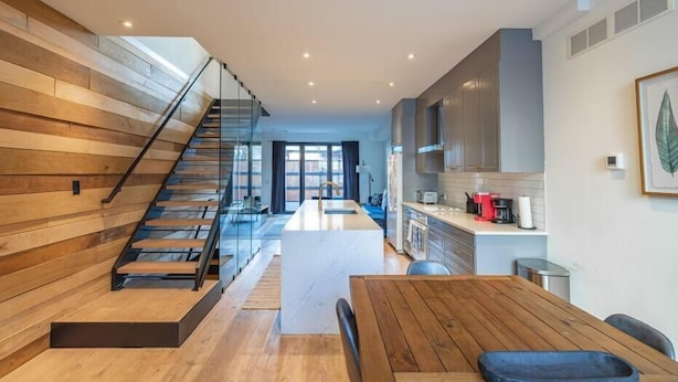 Una cocina moderna con suelo de madera, una isla central y una escalera con barandillas de vidrio.