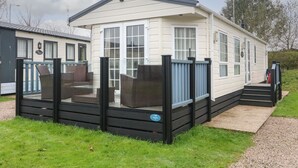 A mobile home with a covered patio, a fenced deck, and a small outdoor seating area. - The Bobbin, Number 11 (Carnforth)