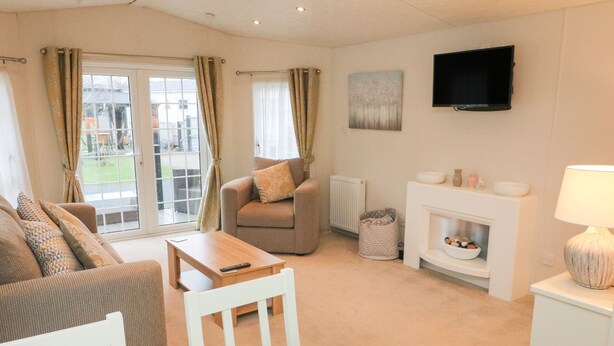 A living room with a sofa, armchair, coffee table, fireplace, television, and a view through a glass door. - The Bobbin, Number 11 (Carnforth)