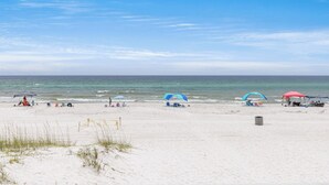 Una playa con sombrillas y sillas, cielo despejado y el océano al fondo.