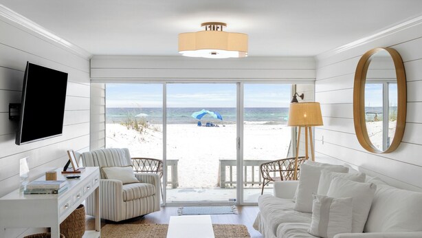 Un salón moderno con vista al mar, muebles blancos, un televisor de pantalla plana y un espejo grande.