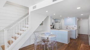 Una cocina moderna con armarios blancos, una isla central y un comedor con sillas transparentes.