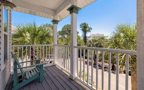A porch with a bench, white railings, and palm trees.