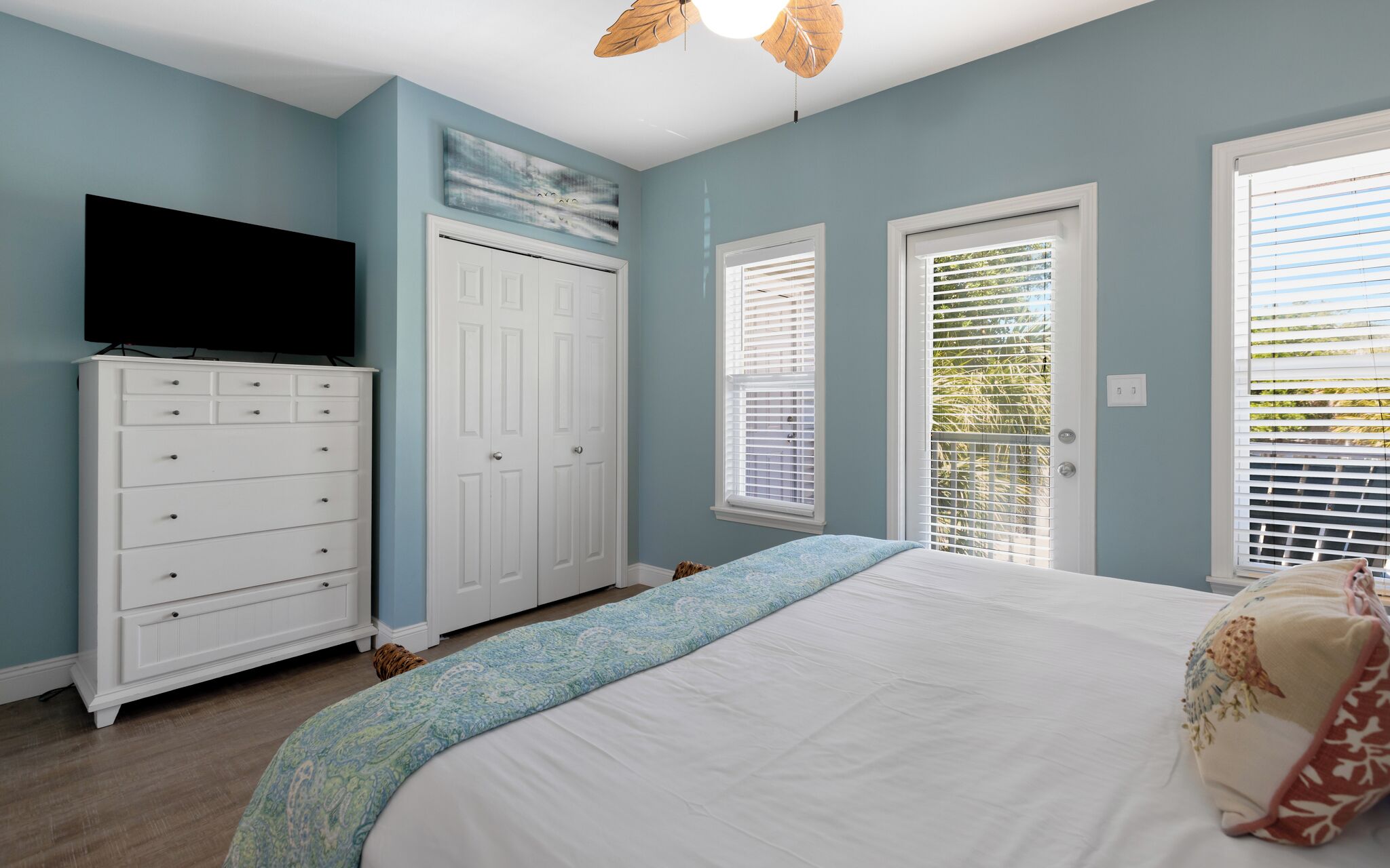 A bedroom with a bed, dresser, television, and two doors with windows.