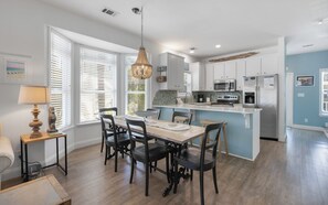A modern kitchen with white cabinets, a central island, and a dining area with a table and chairs.