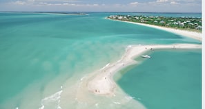 An aerial view of a beach with clear turquoise waters, a sandy shoreline, and a small boat anchored near the shore.