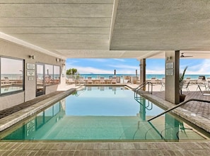 Une piscine intérieure offrant une vue dégagée sur l’océan, des chaises longues et un plafond en béton.