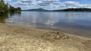 A calm lake with a sandy beach and a forested hill in the background. - New Cabin in Eustis.Mtn, River & Dam Views (Eustis)