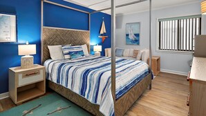 Una cama con dosel con colcha a rayas, una mesita de noche con lámpara, una mesita auxiliar de madera y una ventana con persianas verticales.
