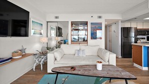 Una sala de estar moderna con un sofá, una mesa de centro y objetos decorativos. Incluye una zona de cocina con electrodomésticos y un refrigerador.