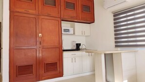 Een keuken met houten kastjes, een magnetron en een raam met jaloezieën.