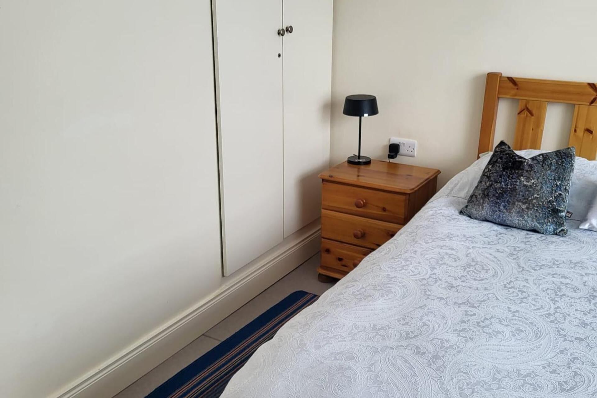 A bedroom with a bed, a wooden nightstand with a lamp, a dresser, and a wardrobe.