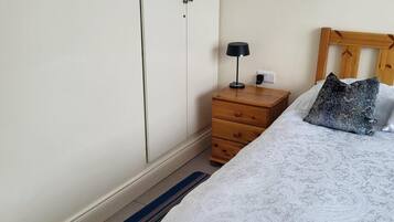A bedroom with a bed, a wooden nightstand with a lamp, a dresser, and a wardrobe.