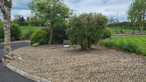 A gravelly landscaped area with a small rock feature, surrounded by trees and shrubs. - 1 Bed Retreat-sleeps 2-secure Parking-garden (Ennis)