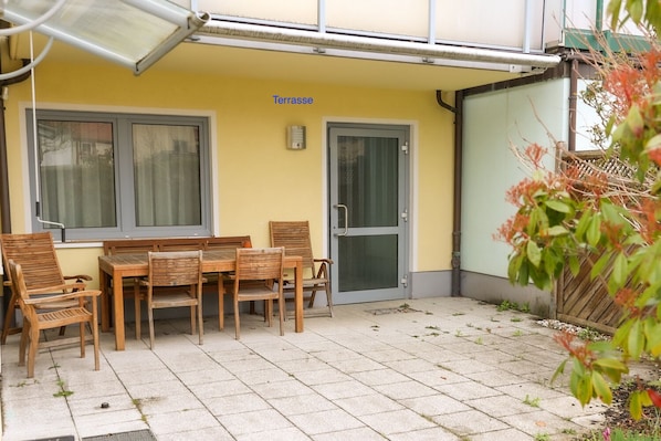 An outdoor terrace with a table and chairs, a door, and a window.