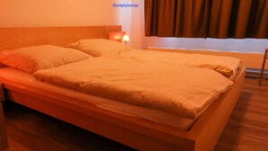 Una cama doble con estructura y cabecera de madera, una mesita de noche con lámpara y una ventana con cortinas.