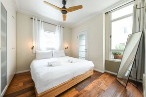 A bedroom with a bed, a ceiling fan, a window with curtains, and a view of greenery outside. - Stylish and Modern 3BR TelAviv Apartment (Tel Aviv)