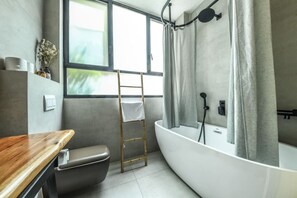 A modern bathroom with a bathtub, a toilet, a vanity with a mirror, and a window providing natural light. - Stylish and Modern 3BR TelAviv Apartment (Tel Aviv)