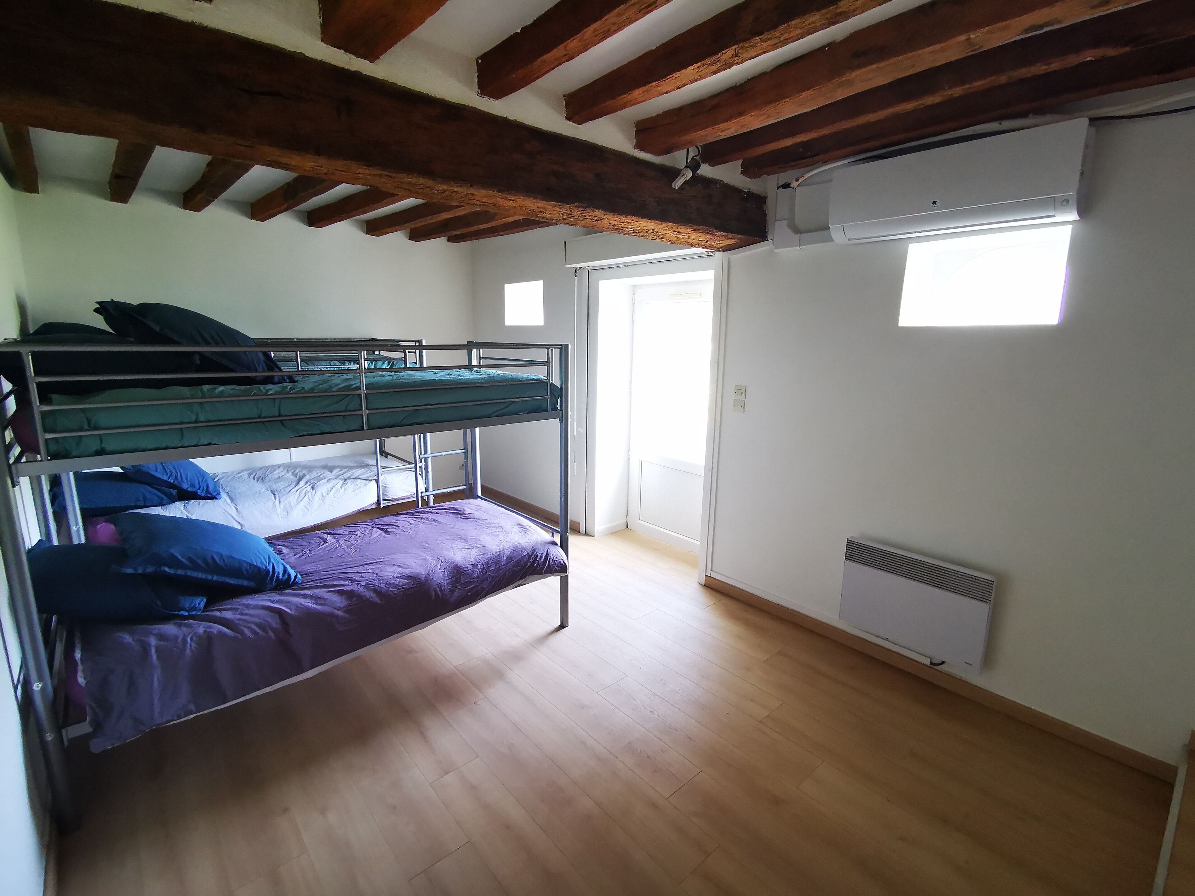 A room with a bunk bed, wooden beams on the ceiling, a window, and a radiator.