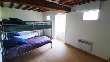 A room with a bunk bed, wooden beams on the ceiling, a window, and a radiator.