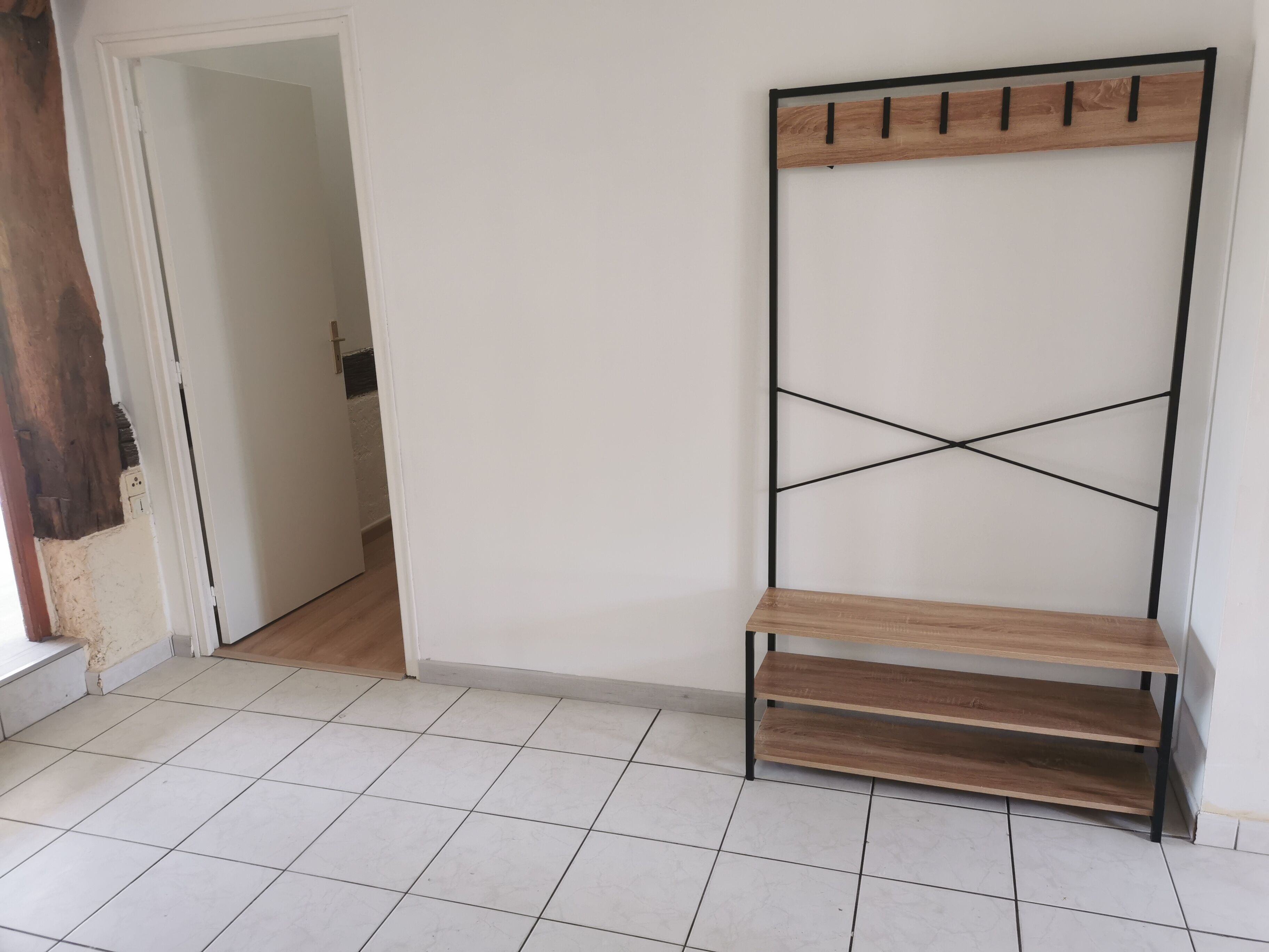 A room with a white tiled floor, a wooden bench with a metal frame, and a door leading to another room.