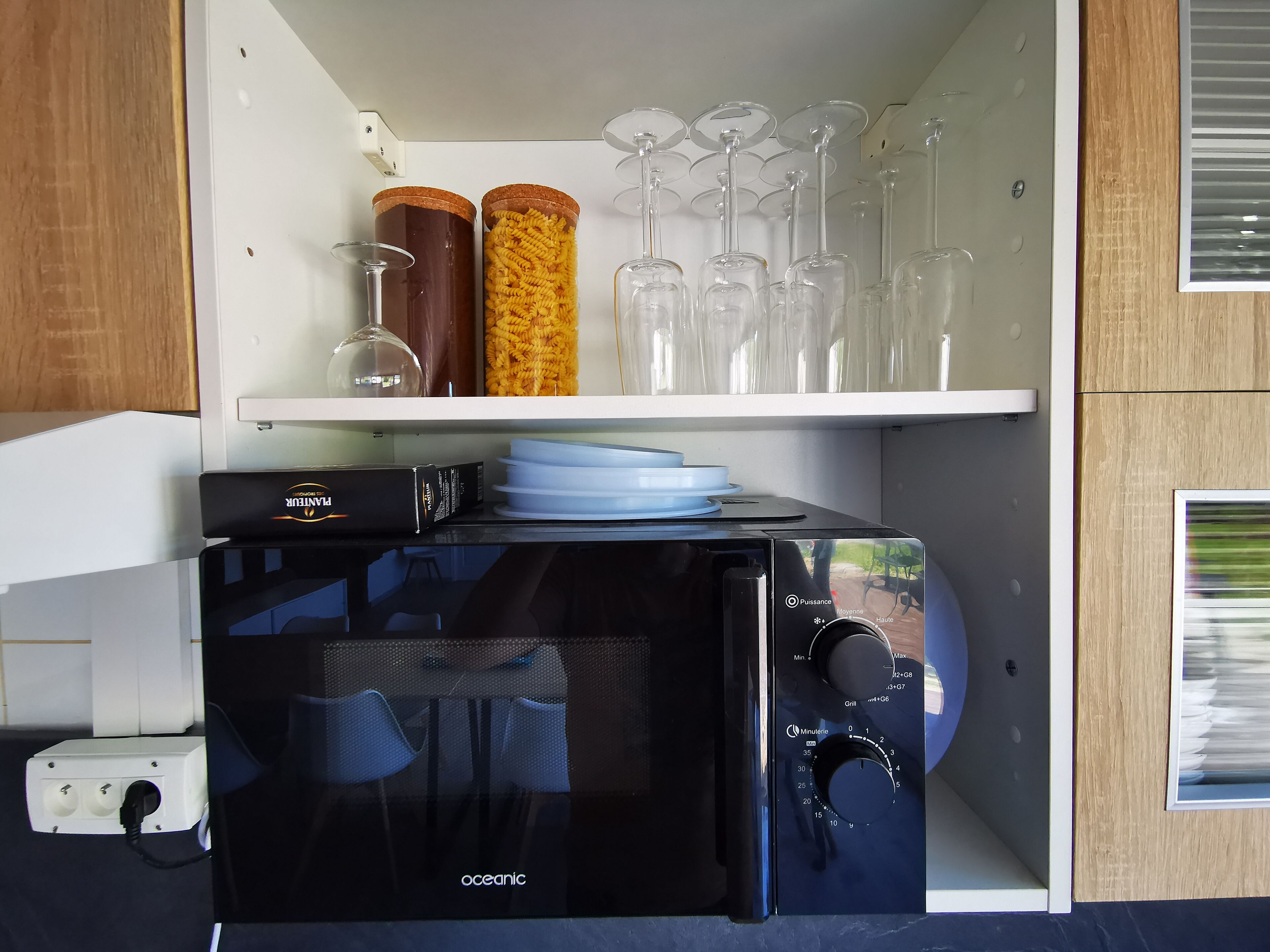 Una piccola cucina componibile con un forno a microonde nero, un piccolo forno e uno scaffale con bicchieri da vino e contenitori per la pasta.