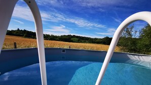 En klarblå pool med utsikt över ett fält och träd i bakgrunden.